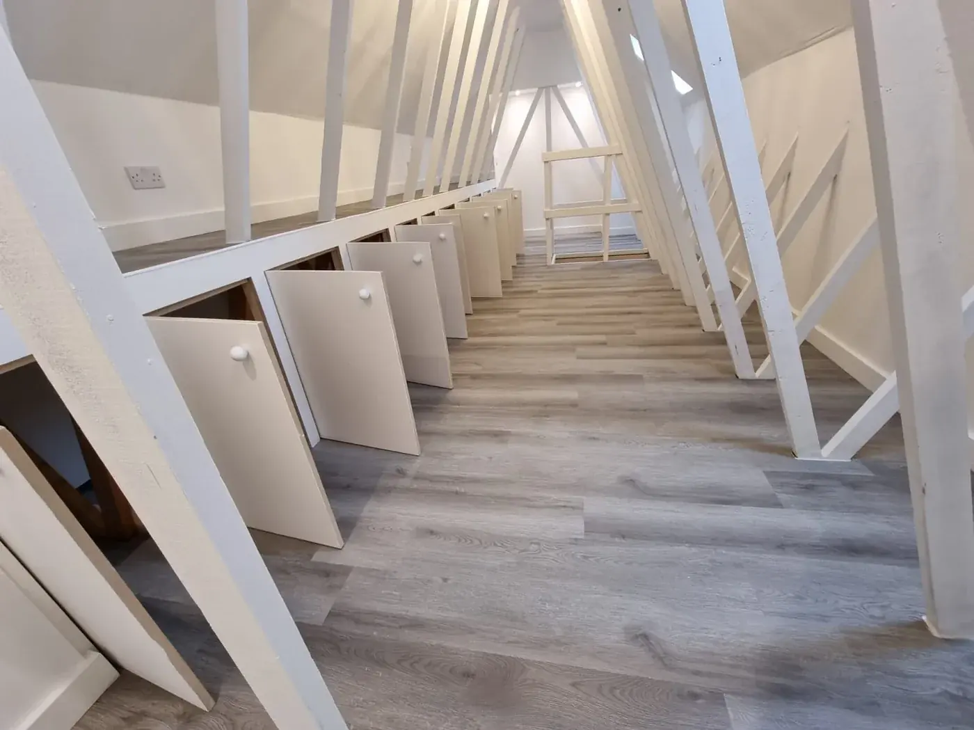 A finished RJ loft storage room with white-painted timbers, handmade fitted cupboards and wood-effect flooring